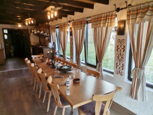a long table and chairs in a room with windows at Къща за гости РАЙ 10човека in Boykovtsi