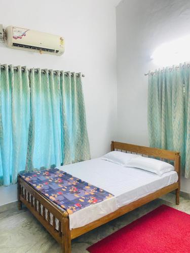 a bed in a room with blue curtains and a red rug at Mampilly Guest House in Kottayam