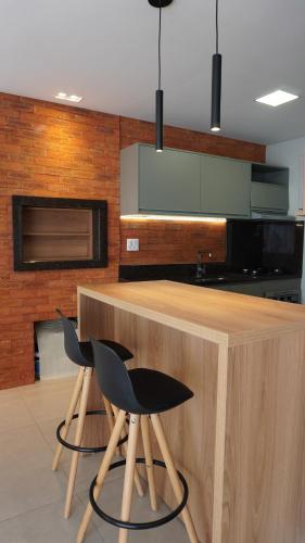 a kitchen with a counter with two black chairs at Casa 2 suítes, ofurô, piscina no Vale dos Vinhedos in Monte Belo