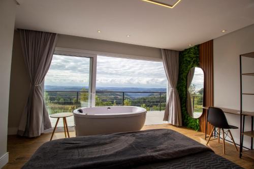 a bedroom with a tub and a large window at Casa 2 suítes, ofurô, piscina no Vale dos Vinhedos in Monte Belo
