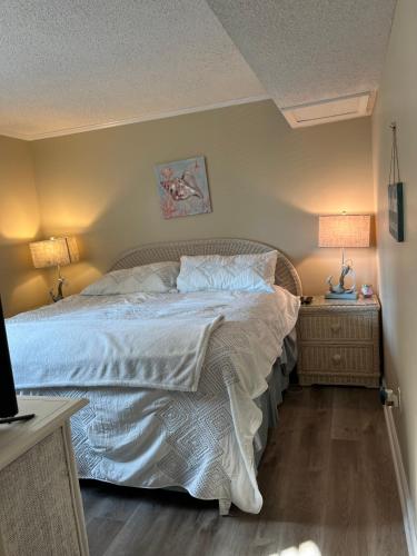 a bedroom with a bed with white sheets and two lamps at Cherry Grove condo just steps from the ocean in Myrtle Beach