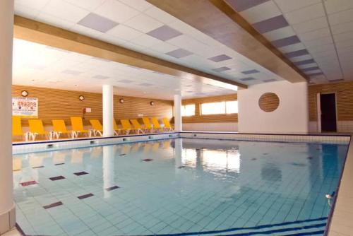 - une grande piscine avec des chaises orange dans un bâtiment dans l'établissement Cocon des Orres res balcon des airelles appartement 512, aux Orres