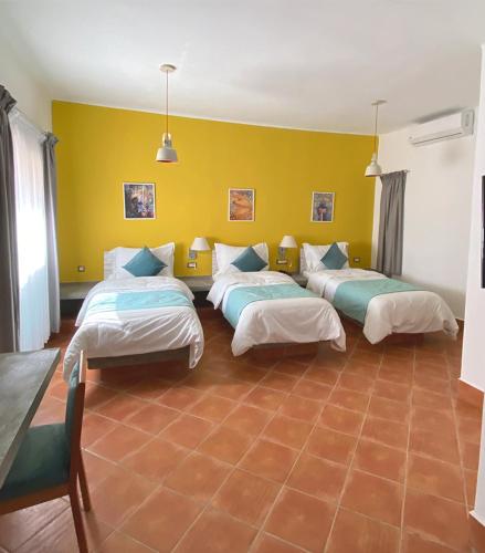 a room with three beds and a yellow wall at Le relais des sables in Tatta
