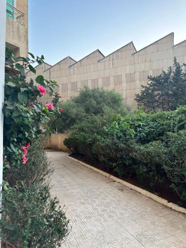 a brick walkway in front of a building with pink roses at Baie d'Alger in Husseïn Dey