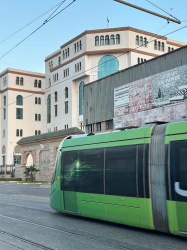 a green train driving down a street in front of a building at Baie d'Alger in Husseïn Dey