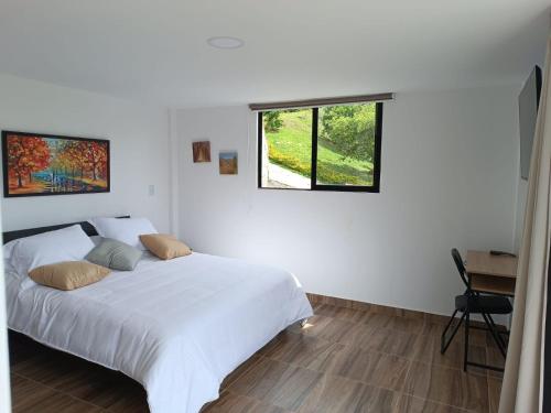 a white bedroom with a bed and a window at Cabaña Estancia Primavera in Guatapé