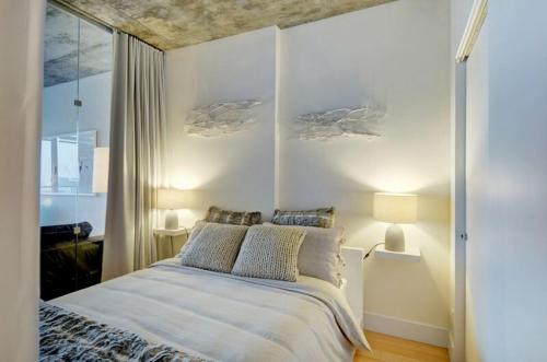 a white bedroom with a bed and two pillows at Les Immeubles Charlevoix - Le 760214 in Quebec City