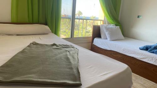 Habitación con 2 camas y ventana con cortinas verdes. en Chalet Blumar eldom elsokhna, en Ain Sokhna