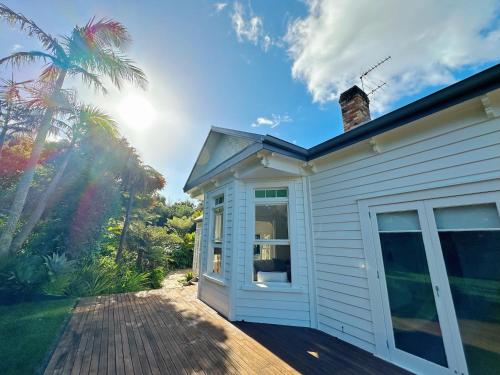 a white house with a porch and a palm tree at The Ultimate Escape - Holiday Villa Private POOL in Auckland