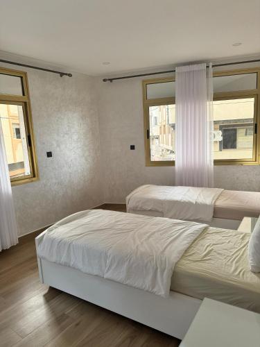 two beds in a bedroom with two windows at Belle cote appartement al hoceima in Al Hoceïma