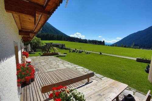 a wooden deck with a bench and a field of grass at Aussermahrhof - familyfarm in Gsies