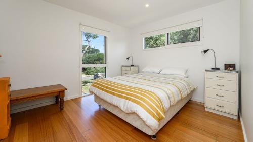 Un dormitorio blanco con una cama y dos ventanas. en Classic 70's Beach House Outside - 97-99 Lohr Avenue, en Inverloch