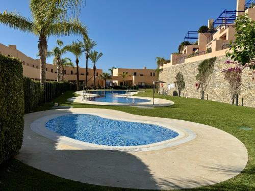 una piscina en un patio con palmeras y edificios en Darwins Luxury Mojácar, en Mojácar