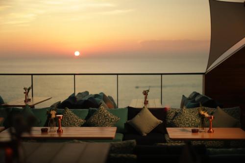 a room with a couch and tables with the sunset in the background at Raouche Arjaan by Rotana in Beirut