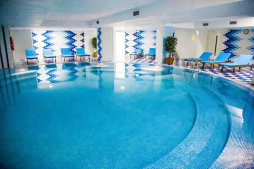 une grande piscine dans un hôtel avec des chaises bleues dans l'établissement Ramada by Wyndham Almaty, à Almaty