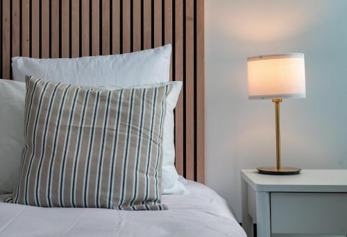 a bed with a striped pillow and a lamp on a table at Résidence Jaures - Appartements design et climatisés en centre ville in Vichy