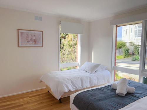 two beds in a white room with a window at Sunny Retreat House in Hobart