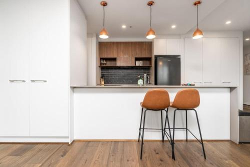 een keuken met witte kasten en 2 stoelen aan een balie bij Stylish 2BR Apt 5 mins to Canberra Hospital - Hosted by Canstay in Phillip