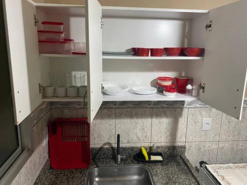 a kitchen with a sink and red bowls and plates at Aptos 1 quarto Ar Saraiva in Uberlândia