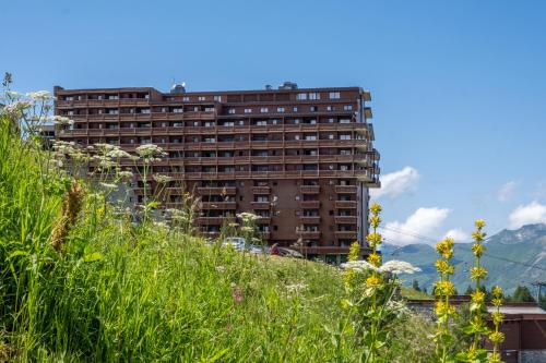 un grand bâtiment sur une colline avec de l'herbe et des fleurs dans l'établissement Résidence Pierre & Vacances Premium Les Hauts Bois, à Aime La Plagne