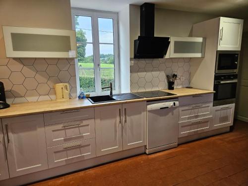 une cuisine avec des armoires blanches, un évier et une fenêtre dans l'établissement Gîtes à la ferme, à Maux