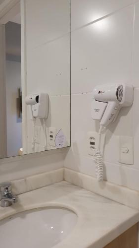 a bathroom sink with a mirror and a hair dryer at Astron Suítes Mondial Salvador by Nobile in Salvador