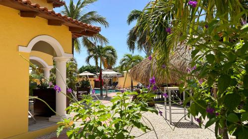 a yellow building with a patio with tables and palm trees at Sonrisa Boutique Hotel - Adults Only in Kralendijk