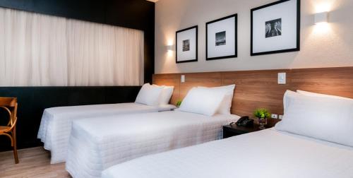 two beds in a hotel room with white sheets at Cambirela Hotel in Florianópolis