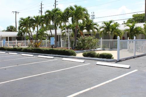 a parking lot with a white fence and palm trees at Economy Inn in West Palm Beach