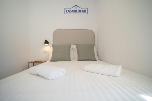 a white bed with two pillows and a sign on it at Sanlucar Centro - Apartamento 5 in Sanlúcar de Barrameda