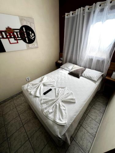 a bedroom with a bed with white sheets and a window at Pousada Morada Dusanjos in Caraguatatuba