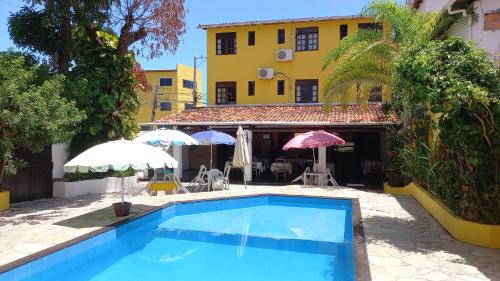a swimming pool in front of a house with umbrellas at Pousa Hotel Sonho de Verão in Vera Cruz de Itaparica