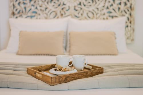a tray with two cups and cookies on a bed at La Casetta della Nonna in Lardos