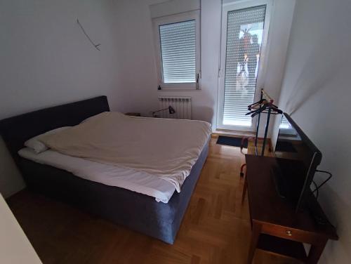 Un dormitorio con una cama y una mesa y dos ventanas. en Room in a nice sunny apartment, en Vračar (historical)