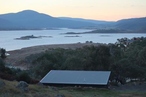a barn on a hill next to a body of water at Hygge Eco Cabins Beautiful New Cabins with Amazing Views in Jindabyne