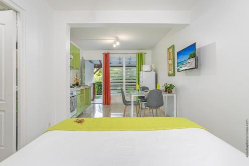 a bedroom with a white bed and a kitchen at Anis au Refuge de Madiana à Schoelcher in Schœlcher