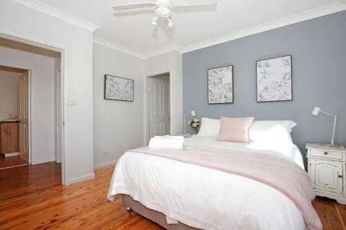 a bedroom with a large white bed with a ceiling fan at Queen Street Cottage - By Berry Getaways in Berry
