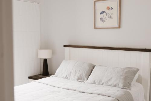 un letto con lenzuola bianche e una foto sul muro di Marcoola Beachside Resort a Marcoola