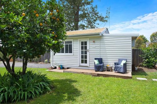 a small white house with two blue chairs in a yard at Fremily Cottage - By Berry Getaways in Berry