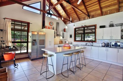 a kitchen with white cabinets and a island with bar stools at Amaroo House - By Berry Getaways in Berry