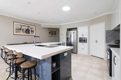 a kitchen with white cabinets and a large island with stools at Endless Entertainment on the Coast - A Family Oasis in Mornington
