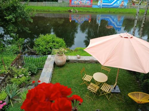 - une table et des chaises avec un parasol en face d'un étang dans l'établissement Maison de charme en bord de Jordanne, à Aurillac