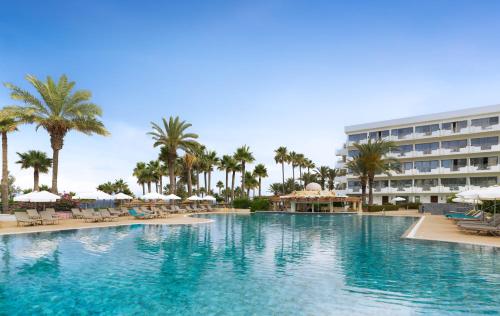 a large swimming pool with palm trees and a hotel at St George Beach Hotel & Spa Resort in Paphos
