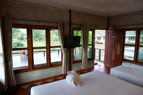 a bedroom with two beds and a television and windows at Nok Chan Mee Na in Chom Thong