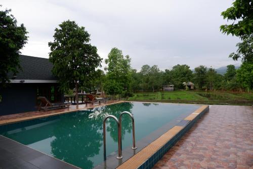a swimming pool with two metal railings in front of a house at Nok Chan Mee Na in Chom Thong