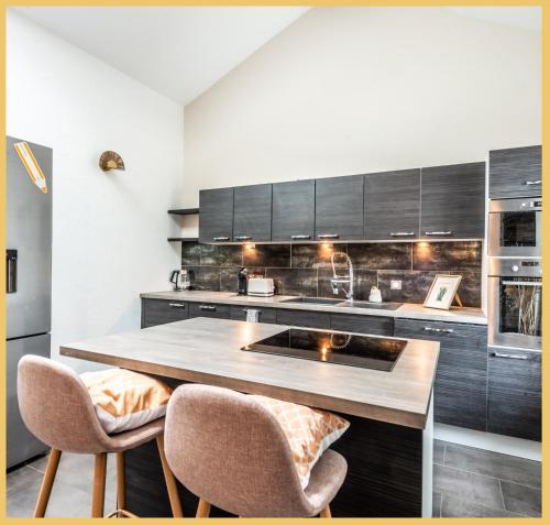 une cuisine avec des armoires noires et un comptoir avec deux chaises dans l'établissement Chez Douv I T2 I Douvaine, à Douvaine