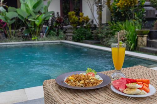 a table with two plates of food and a glass of orange juice at Campuhan Guesthouse in Tabanan