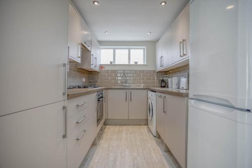a large kitchen with white cabinets and a window at Cockle Cottage - Crabpot Cottages in Cromer