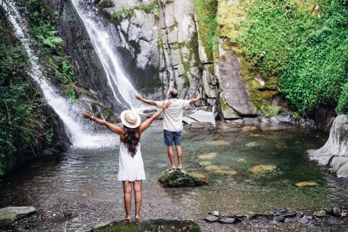 a man and a woman standing on a rock in front of a waterfall at Story Studio Piódão - Heritage in Piódão