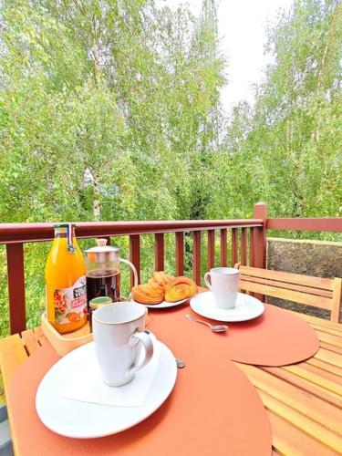 a table with two cups and plates of food on a deck at L'écrin paisible - Balcon sur ruisseau, vue montagne & parking in Bielle